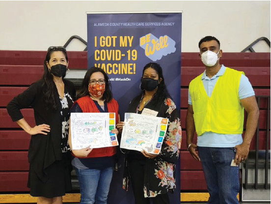 four masked people pose for a picture at a vaccine event